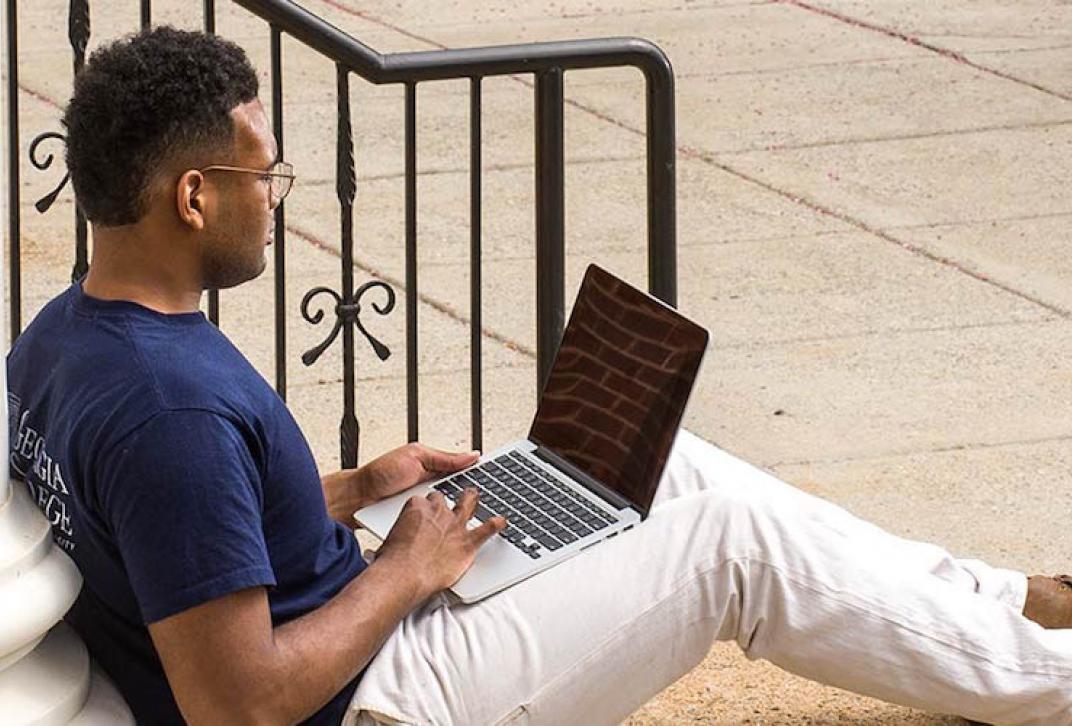adult student on laptop leaning against a column