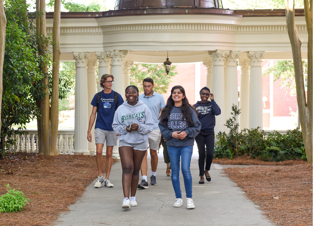A group of students walk on through the pergola on campus.