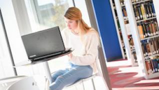 student on laptop in library near window