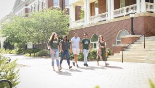 A group of students walks on the sidewalk outside of Atkinson Hall.