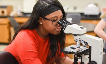 student peering through microscope in lab