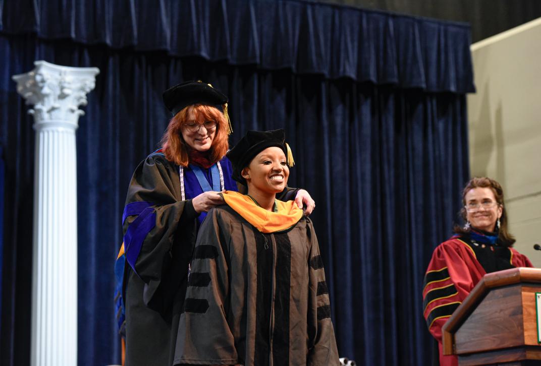 A Nursing doctoral student receives her graduate hood from her academic advisor during the commencement ceremony.