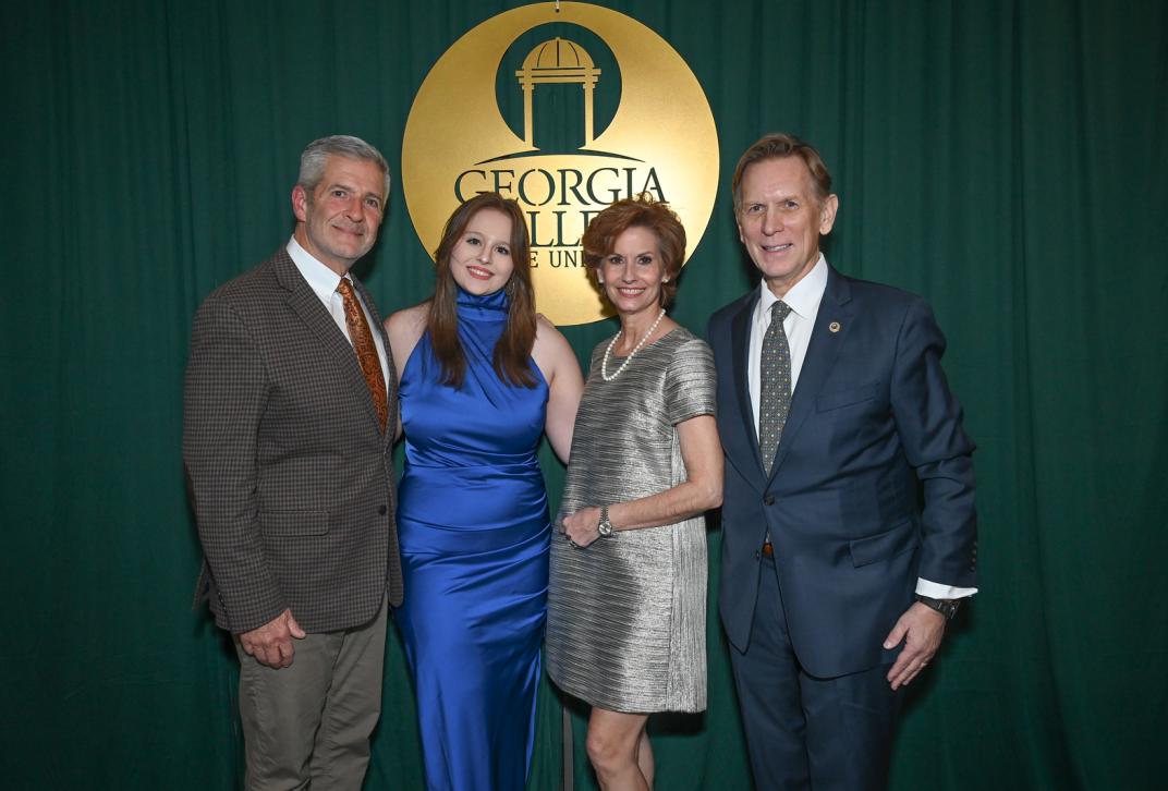 Alumni and guests stand in front of green and gold backdrop at the Alumni Awards 