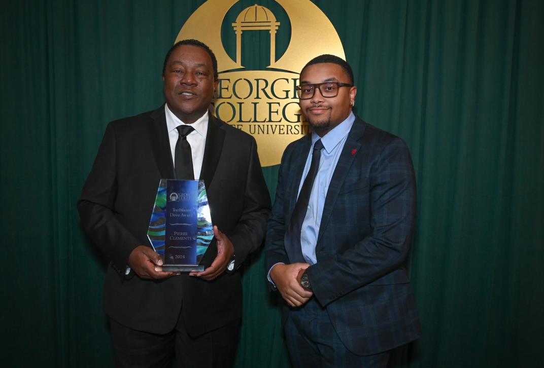 Alumni and guests stand in front of green and gold backdrop at the Alumni Awards 