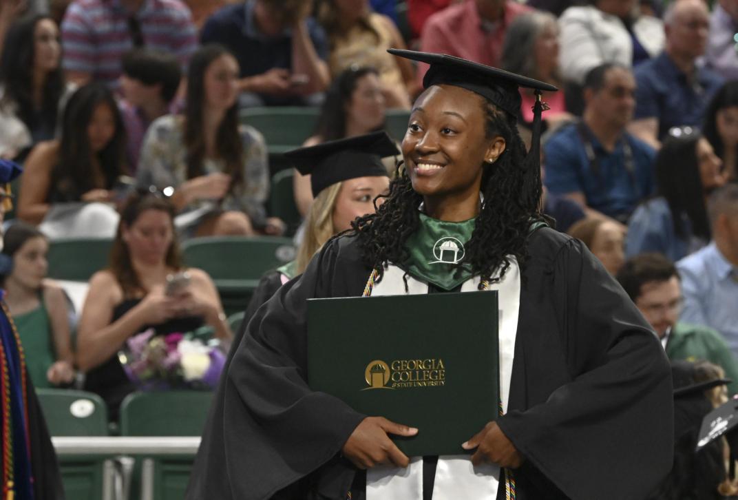 Student poses with diploma cover during commencement ceremony.