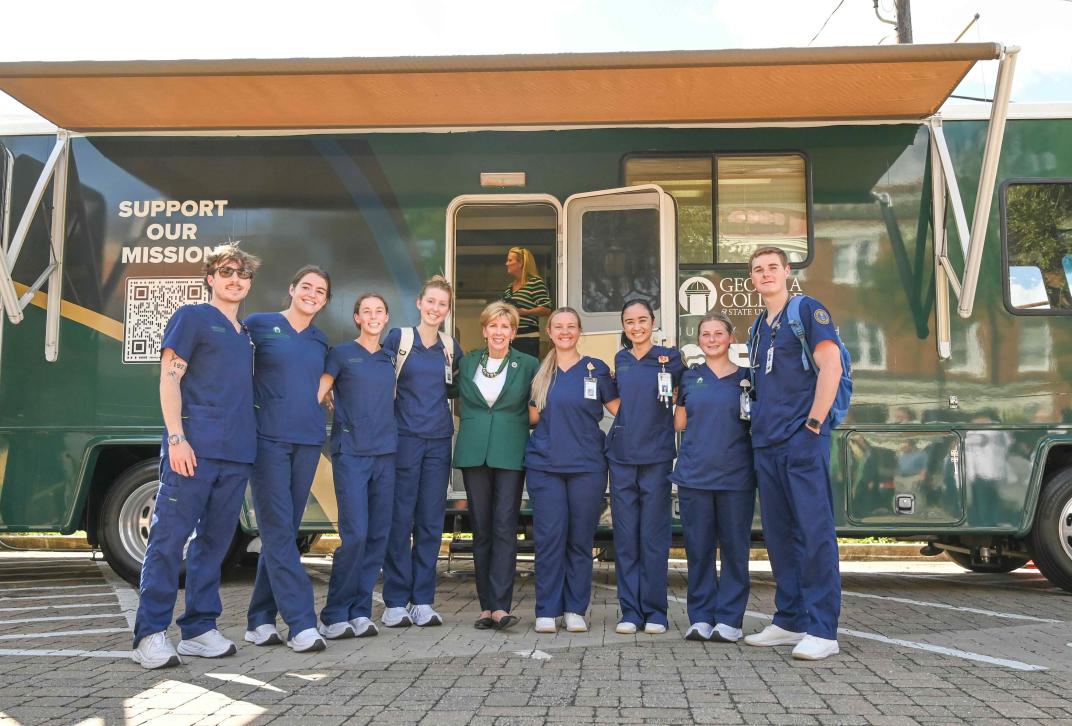 Picture of GCSU President Cox and students in front of the Mobile Health Unit.