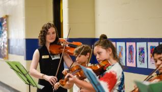 A GCSU students shows elementary students how to play violin