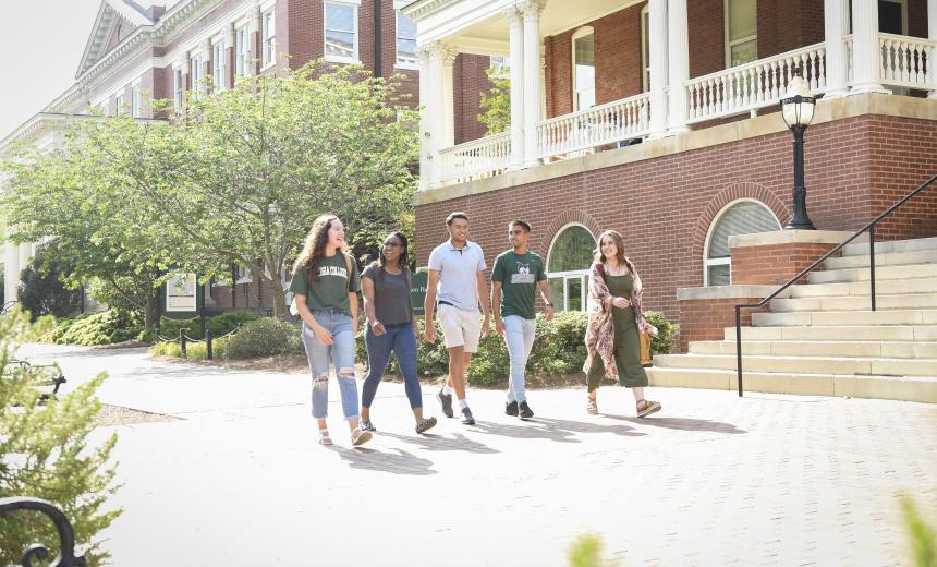 A group of students walks on the sidewalk outside of Atkinson Hall.