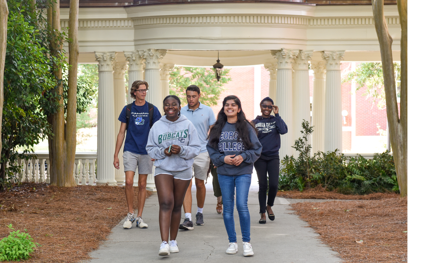A group of students walk on through the pergola on campus.