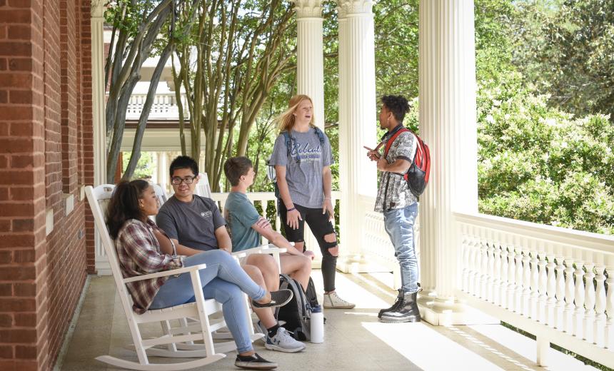 A group of students sit and talk on the porch of Atkinson Hall.