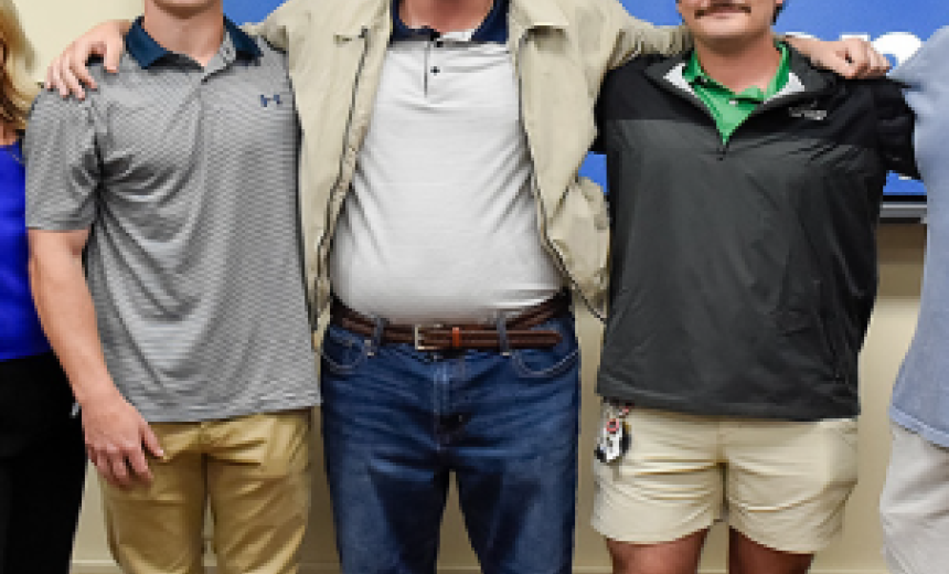 Three students pose for a photo in front of large TV screen