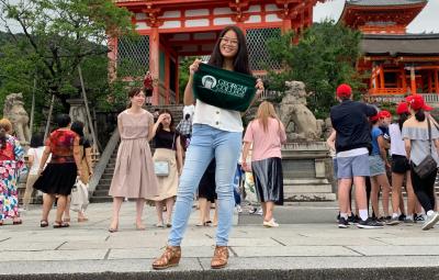 A student poses with a Georgia College green towel in front of a castle in Japan