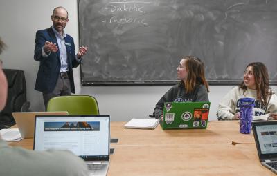 A professor teaches at the chalkboard while students listen and learn in a classroom