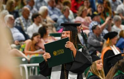 A student holds up their diploma and celebrates at commencement
