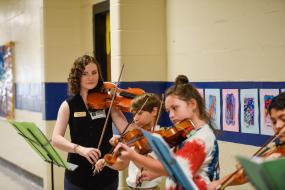 A GCSU students shows elementary students how to play violin